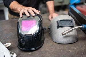 A very strong conceptual image on workplace safety, the strong hand of a worker rests on a modern welder's helmet. On the sides a work glove and the tip of the welding machine. photo