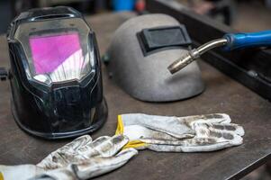 A conceptual image about safety at work, a modern welding helmet and a vintage one next to it. On the sides a work glove and the tip of the welding machine. photo