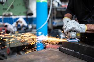 Using the flexible disc grinder on a metal bar, when the tool touches the surface, numerous orange sparks are projected. Concept of metal processing in the workshop. Craft work, metal working. photo