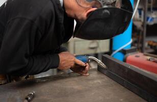Conceptual image of a blacksmith busy using the welding machine. Place the tip of the soldering iron on the point to be fixed. Blurred workshop background. Welding, repair, work concept. Copy space photo