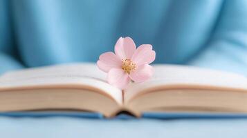 Open Book with a Delicate Pink Flower on Pages Against a Soft Blue Background for Inspirational Themes photo
