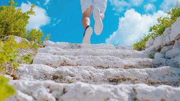 Person Climbing White Stone Steps Under Bright Blue Sky Surrounded by Lush Greenery and Clouds photo