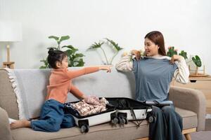 Travel Planning and Cooperation. A girl excitedly points at clothes while sharing a packing moment with her mother. photo