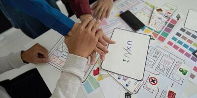 Collaboration and UX UI Design. Team members unite hands over design concepts, emphasizing teamwork in the UX UI design process. photo