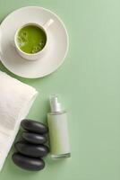 Overhead view of matcha tea, spa stones, towel, and a green dropper bottle photo