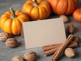 Blank card surrounded by orange pumpkins, walnuts, and cinnamon sticks on a rustic gray surface photo