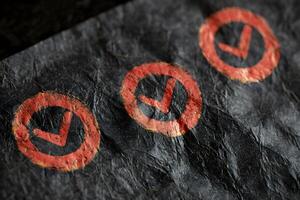 Red Checkmarks on Crumpled Dark Paper Background Texture photo