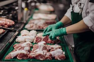 Butcher preparing raw meat cuts on a processing line wearing gloves photo