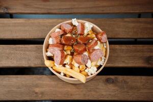 Poutine fries with chees and sausage in paper takeout container. Delicious freshly prepared meal, perfect for menus, restaurants, or food delivery concepts. photo