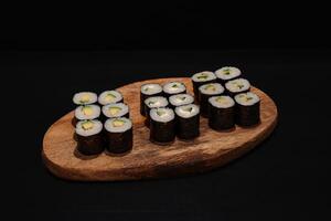 Creative minimalist display of assorted Maki sushi rolls on a wooden platter against a dark backdrop, emphasizing vibrant colors and exquisite Japanese culinary art with a modern aesthetic. photo