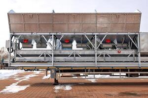 Large metal containers with red vibrators and shakers rest on a trailer in a snowy yard on a cold winter day. photo