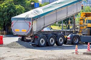 Construction activity showcases a truck unloading gravel at a busy intersection during the daylight. Copy space. photo