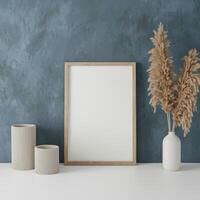 Minimalist interior scene with a blank frame, vases, and dried plant, set against a blue wall. photo