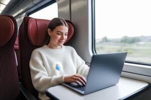 Woman working on her laptop during a train ride, looking out the window at the passing scenery. photo