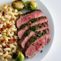 Plate with medium-rare sliced steak, pasta, and Brussels sprouts, a balanced and savory meal. photo