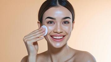 Smiling woman with clear skin applies product with cotton pad, promoting skincare routine. photo