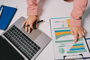 A person is using a laptop with graphs and papers photo