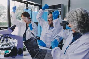 Three people in lab coats and gloves are working on a laptop photo