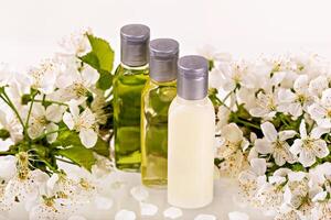 Three natural cosmetic bottles with silver caps stand among fresh white blossoms. Delicate floral setting enhances concept of organic beauty, skincare and relaxation with soft, luxurious aesthetic photo