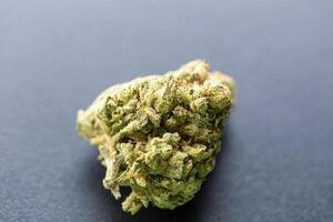 Close-up of single cannabis bud on dark background with visible trichomes and natural texture, isolated with soft lighting. Concept of medical marijuana, CBD products, or herbal wellness photo