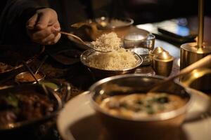Indian dish chicken curry, in the background a man's hand is pouring rice with spoon photo