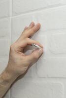 man's hand holds a dowel with a screw for mounting near the wall. photo