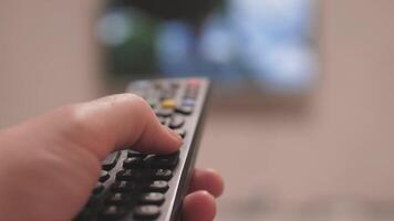 A hand skillfully operating a remote control, pointing at a bright television screen while enjoying entertainment video