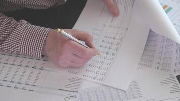 A detailed closeup of hands meticulously writing on financial spreadsheets and reports, showcasing data analysis video