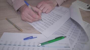 A focused individual meticulously reviews complex financial data using worksheets and various writing tools video