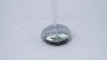 A closeup of clear water cascading over a shiny drain cover, creating soft bubbles and mesmerizing ripples video