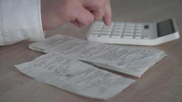 An individual is meticulously reviewing receipts and calculating various expenses with a calculator on a wooden table video