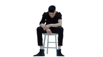 A contemplative individual seated on a stool dressed in black attire with hands resting though png