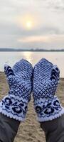 Hands in knitted mittens against the background of a winter landscape and sunset photo