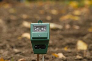 Green soil moisture meter in a garden setting with blurred muddy background, photo