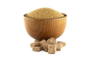 A rustic wooden bowl overflows with raw brown sugar accompanied by neatly arranged sugar cubes. photo