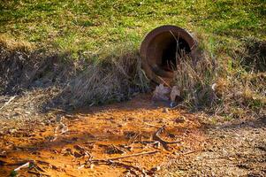 Polluted Water Flowing From a Rusty Drain Pipe Into Contaminated Soil in a Natural Environment photo
