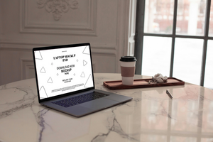Laptop on a marble table with coffee and a window in the background psd