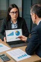 A man and woman in business attire are looking at a laptop screen photo