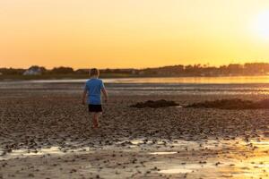 Boy walking on the beach during sunset, exploring the shore at low tide in a tranquil coastal setting photo