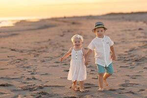Siblings walk hand in hand on the beach during sunset near the ocean in a warm and serene atmosphere photo