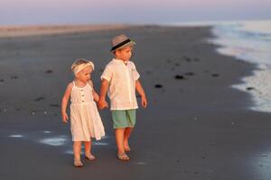 Children explore a serene beach while holding hands at sunset on a warm summer evening photo