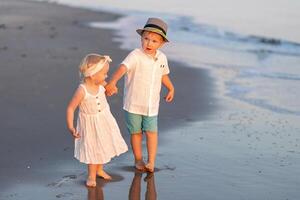 Children walking hand in hand along the shore during sunset at the beach in warm weather photo