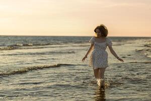 Woman wades through shallow water at sunset on a serene beach surrounded by gentle waves photo