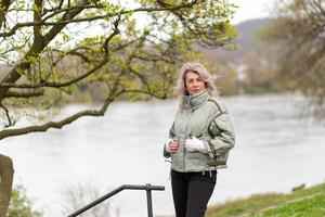 Woman stands by a river in a park wearing a light jacket and enjoying nature on a cloudy day photo