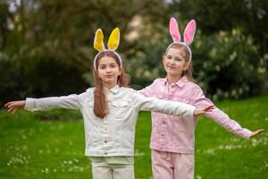 Two girls in bunny ears playfully pose outdoors during spring in a lush green park setting photo