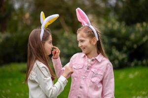 Two children wearing bunny ears share a joyful moment in a park during an Easter celebration on a sunny day photo