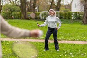 Woman with badminton racket standing in park near a man in the foreground photo