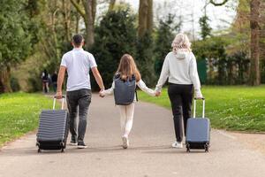 Family of three, father, mother, and daughter, walking in a park with suitcases photo