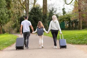 Family of three, father, mother, and daughter, walking in a park with suitcases photo