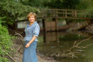 Woman posing by a tranquil riverbank with a wooden bridge in the photo